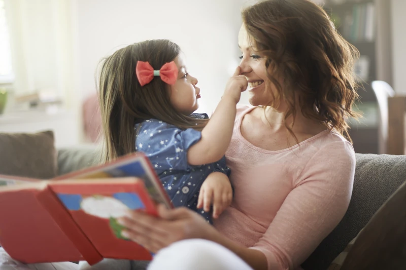 Happy mom holding her daughter and reading a book.